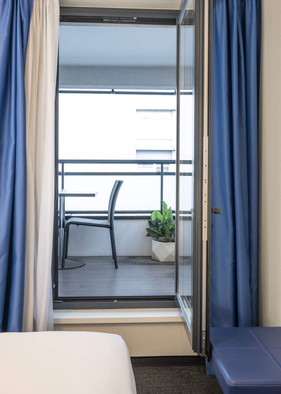 Chambre grand lit avec balcon privatif, table et chaise de jardin à l'hôtel Origami à Strasbourg